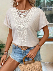 Donna con maglietta bianca in pizzo e shorts di jeans, accessoriata con cintura marrone e borsa di paglia. Look estivo casual chic.