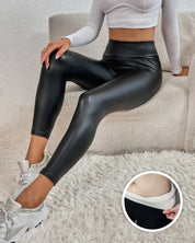 Donna con leggings in ecopelle neri a vita alta, seduta su divano bianco. Dettaglio interno foderato. Abbigliamento moda donna, stile casual chic.