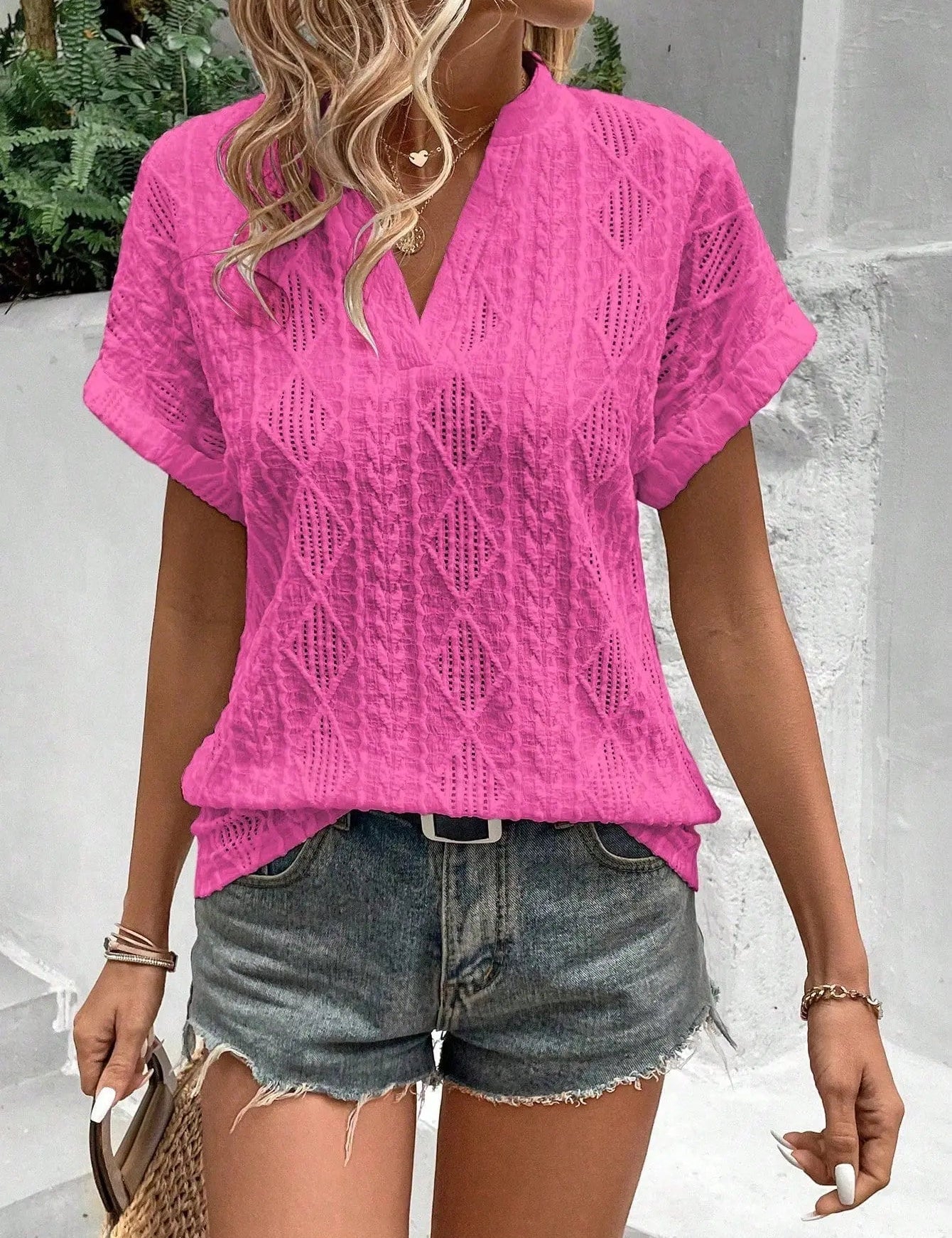 Donna con camicia rosa a maniche corte e pantaloncini di jeans, accessoriata con borsa di paglia. Look estivo casual e alla moda.