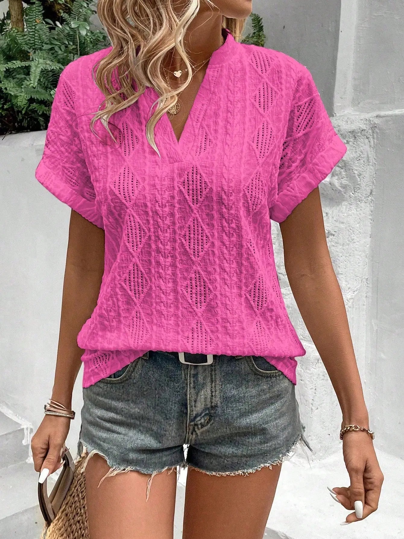 Donna con camicia rosa a maniche corte e pantaloncini di jeans, accessoriata con borsa di paglia. Look estivo casual e alla moda.