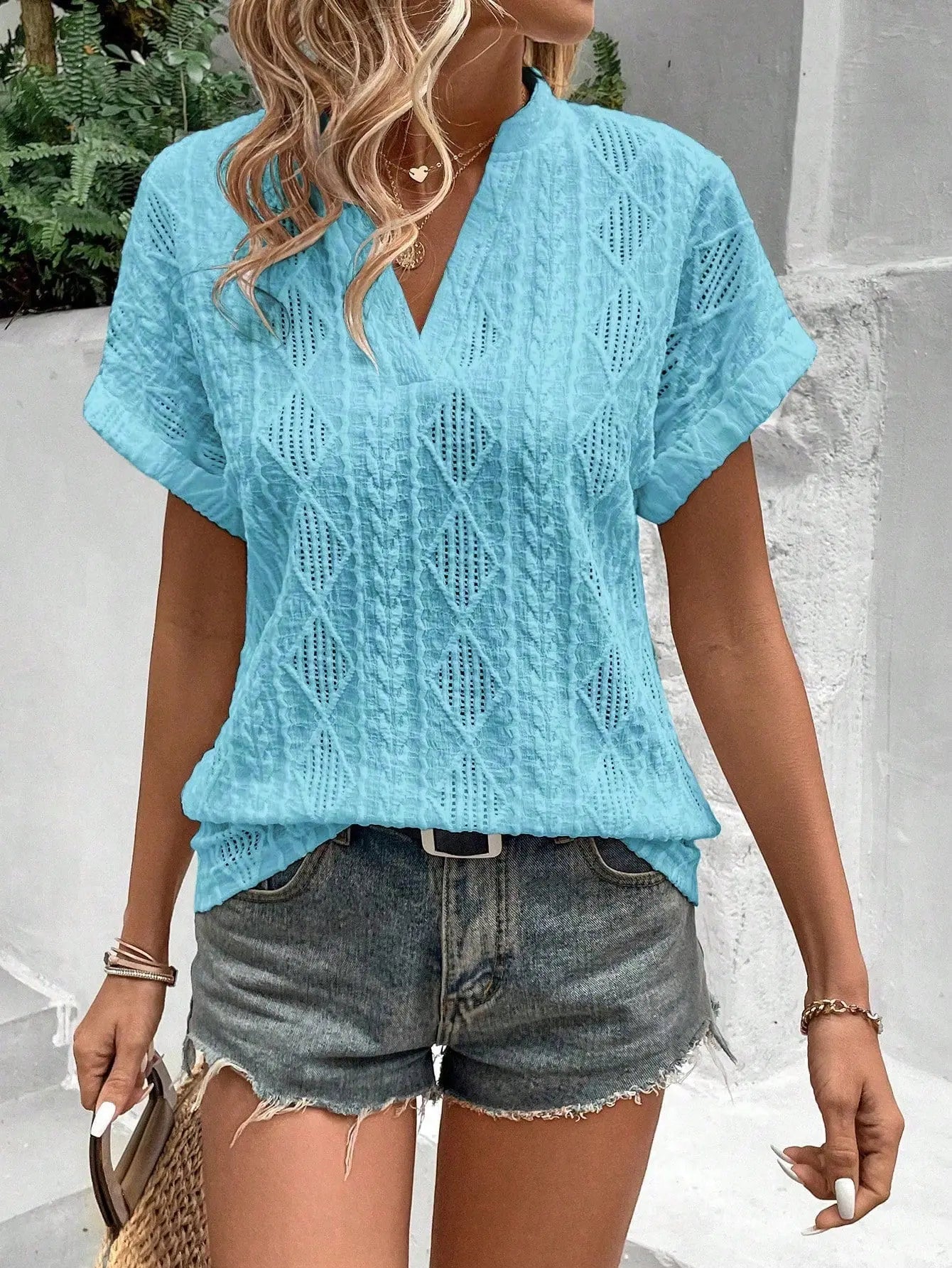 Donna con camicetta azzurra traforata e pantaloncini di jeans, accessoriata con borsa di paglia. Look estivo casual e alla moda.
