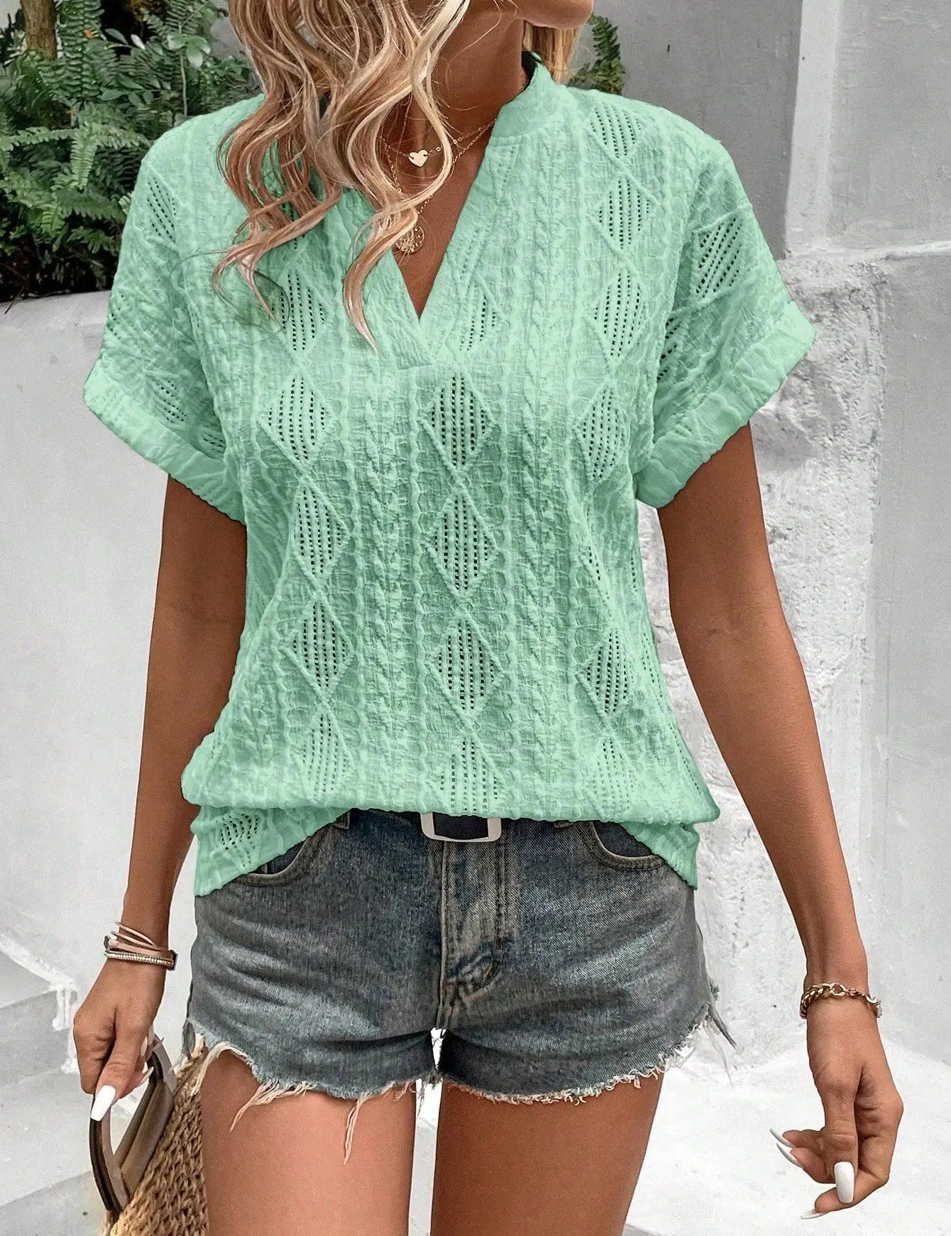 Blusa verde chiaro in cotone con motivo traforato, abbinata a shorts di jeans. Look estivo casual per donna, moda femminile trendy.