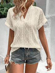 Donna con maglietta bianca traforata e shorts di jeans, accessoriata con borsa di paglia. Moda estiva casual, look fresco e trendy.