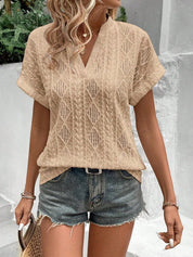 Donna con maglietta beige traforata e pantaloncini di jeans, accessoriata con borsa di paglia. Look estivo casual e alla moda.