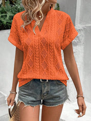 Donna con maglietta arancione traforata e pantaloncini di jeans, accessoriata con borsa di paglia. Moda estiva casual, look trendy e fresco.