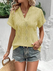 Donna con camicetta gialla traforata e pantaloncini di jeans, accessoriata con collana e borsa di paglia. Look estivo casual e alla moda.