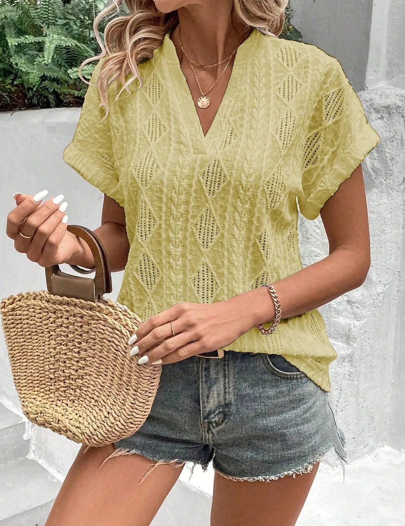 Donna con top giallo traforato, shorts di jeans e borsa di paglia. Moda estiva casual, look trendy, abbigliamento femminile alla moda.