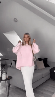 Donna con maglione rosa oversize e gonna bianca in soggiorno moderno. Moda autunnale, abbigliamento casual chic, arredamento minimalista.