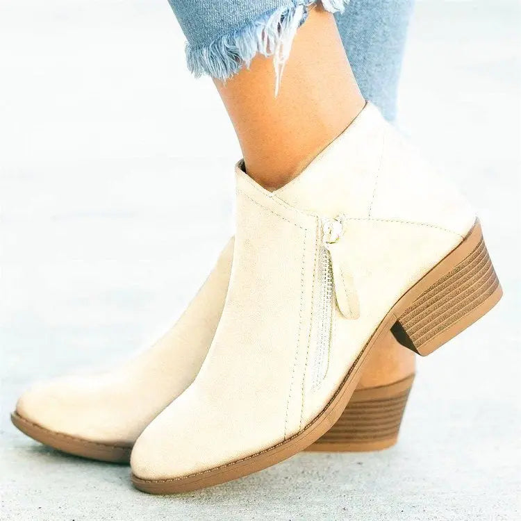 Stivaletti donna beige con tacco basso in legno, zip laterale, indossati con jeans strappati. Scarpe moda autunno, eleganti e casual.