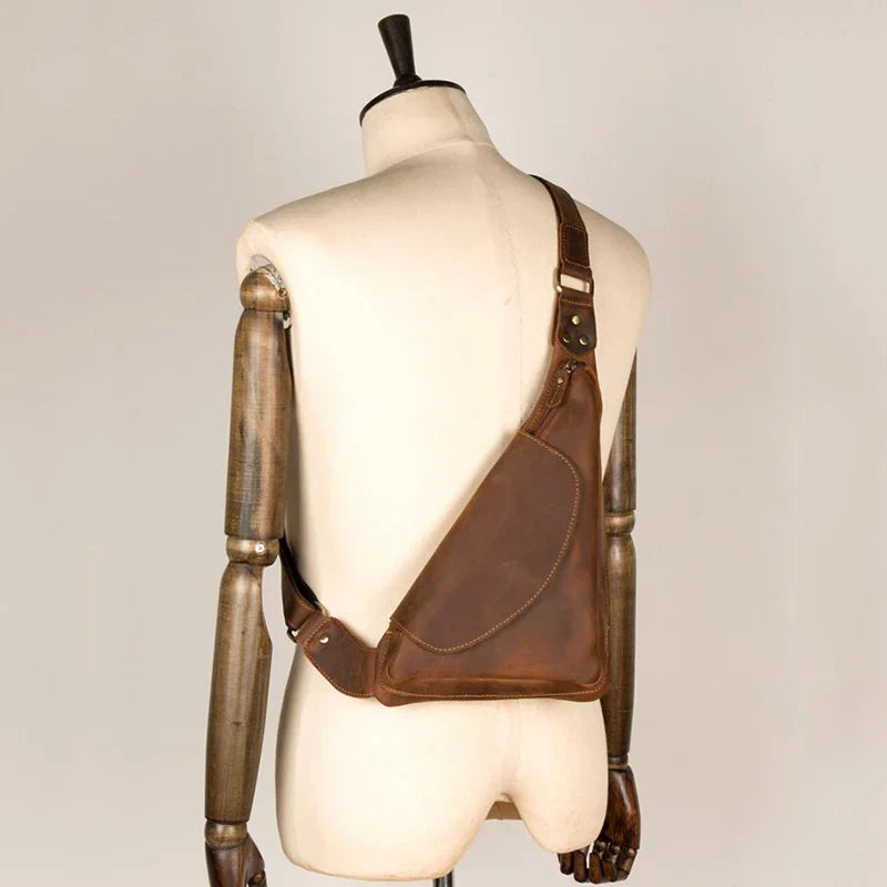 Zaino monospalla in pelle marrone su manichino, design ergonomico, stile vintage, ideale per uomo, accessorio moda, alta qualità artigianale.