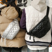 Due persone con giacche imbottite indossano marsupi trapuntati, uno argento e uno nero. Moda urbana, accessori invernali, stile casual.