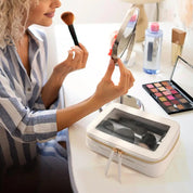 Donna si trucca davanti a uno specchio con pennello, palette ombretti e borsa cosmetica bianca. Routine bellezza, trucco quotidiano, accessori make-up.