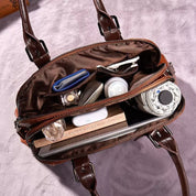 Borsa a tracolla in pelle marrone aperta, mostra scomparti con cosmetici, portafoglio, libro e accessori. Design elegante e funzionale per donna.