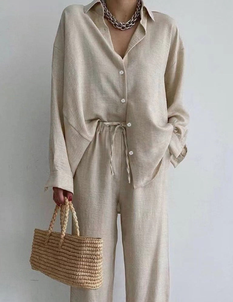 Camicia beige in lino con pantaloni coordinati, collana a catena argento, borsa a mano in paglia intrecciata. Look estivo elegante e casual.