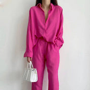 Donna con camicia e pantaloni fucsia, borsa bianca a mano. Moda femminile elegante, abbigliamento casual chic, tendenze colore vivace.