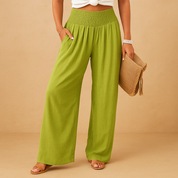 Pantaloni verdi a vita alta da donna, larghi e leggeri, abbinati a top bianco e sandali. Moda estiva casual, accessoriata con borsa in paglia.