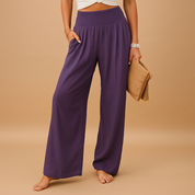 Pantaloni palazzo viola da donna, vita alta, tessuto leggero, abbinati a top bianco e borsa beige. Moda estiva casual elegante.