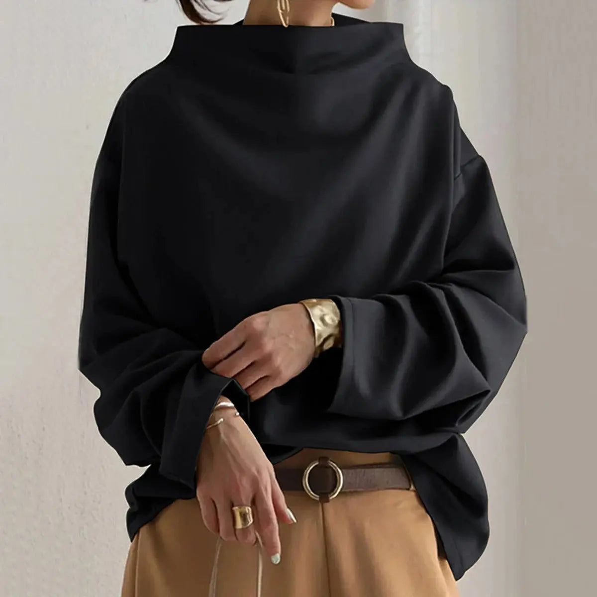Maglione oversize nero da donna, collo alto, maniche lunghe, stile casual chic, abbinato a pantaloni beige e cintura marrone.