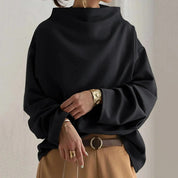 Maglione oversize nero da donna, collo alto, maniche lunghe, stile casual chic, abbinato a pantaloni beige e cintura marrone.