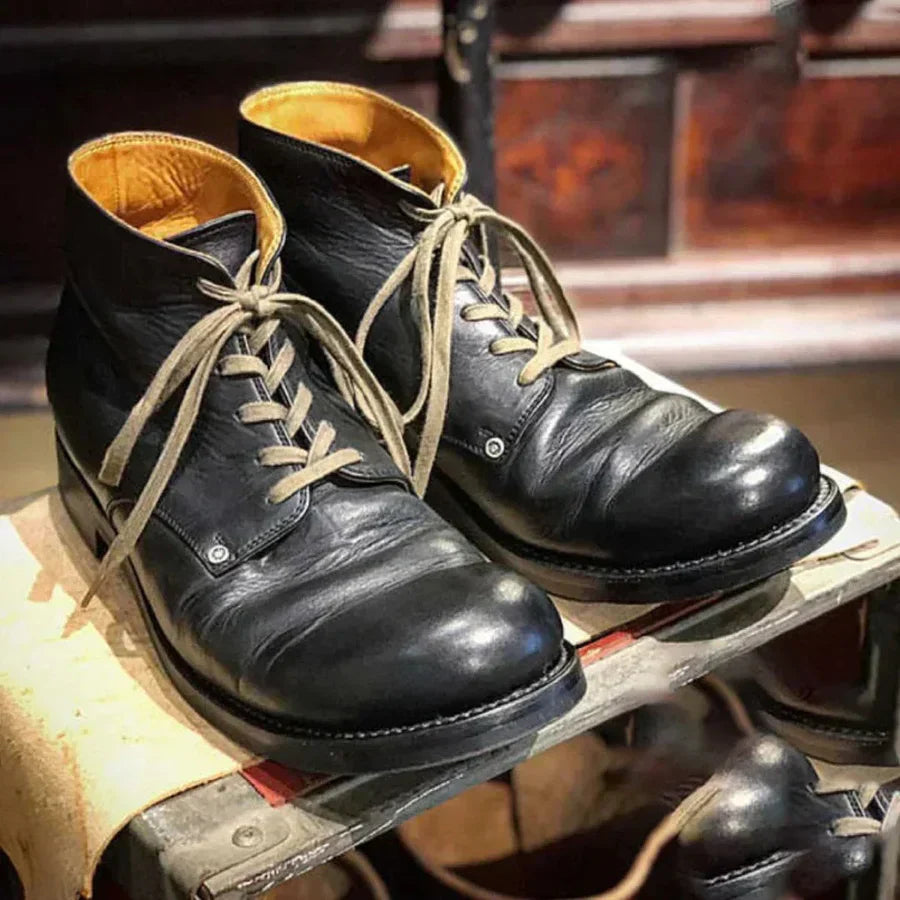 Stivali in pelle nera da uomo con lacci, suola robusta, design vintage, esposti su scaffale in negozio. Scarpe eleganti e resistenti.