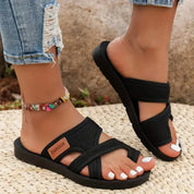 Sandali estivi neri da donna, con design intrecciato e suola in gomma, indossati con jeans strappati e cavigliera colorata.