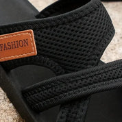 Sandali neri in tessuto traspirante con etichetta marrone "FASHION", suola in gomma, design casual estivo, perfetti per passeggiate all'aperto.