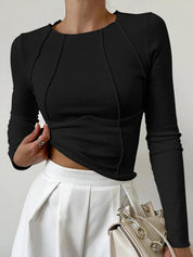 Donna con maglia nera a maniche lunghe e gonna bianca a pieghe, borsa beige con catena dorata. Moda elegante, abbigliamento casual chic.