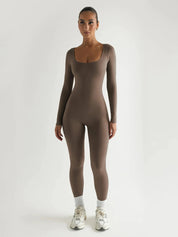 Donna in tuta aderente marrone, maniche lunghe, scarpe da ginnastica bianche, sfondo bianco. Abbigliamento sportivo elegante e moderno.