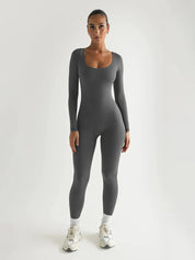 Tuta sportiva grigia a maniche lunghe, donna in posa frontale, scarpe da ginnastica bianche, abbigliamento fitness, moda activewear elegante.