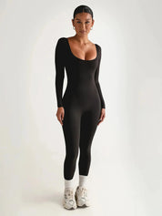 Donna in tuta nera aderente a maniche lunghe, scarpe da ginnastica bianche, sfondo neutro. Abbigliamento sportivo elegante, moda donna.