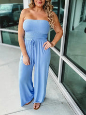 Donna con tuta intera azzurra senza spalline, pantaloni larghi, posa all'aperto. Moda estiva, abbigliamento casual femminile, stile elegante.