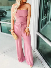 Donna in tuta rosa senza spalline, con borsa di paglia, posa all'aperto. Moda estiva, abbigliamento casual elegante, tendenza 2023.