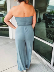 Donna in tuta jumpsuit blu chiaro senza spalline, vista posteriore, davanti a una vetrina. Abbigliamento estivo casual, moda femminile elegante.