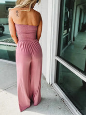 Donna in tuta rosa senza spalline, tessuto elasticizzato, posa all'aperto vicino a una vetrina. Abbigliamento estivo elegante e casual.