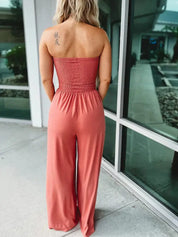 Donna di spalle con tuta rosa senza spalline, tatuaggio sulla spalla, davanti a una vetrina. Moda estiva, abbigliamento casual femminile.