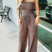 Donna in tuta marrone senza spalline, elegante e casual, davanti a una vetrina. Abbigliamento estivo femminile, moda urbana.