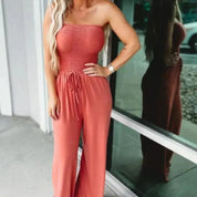 Donna con tuta rossa senza spalline, capelli biondi ondulati, riflessa in una vetrina. Moda estiva, abbigliamento casual elegante.