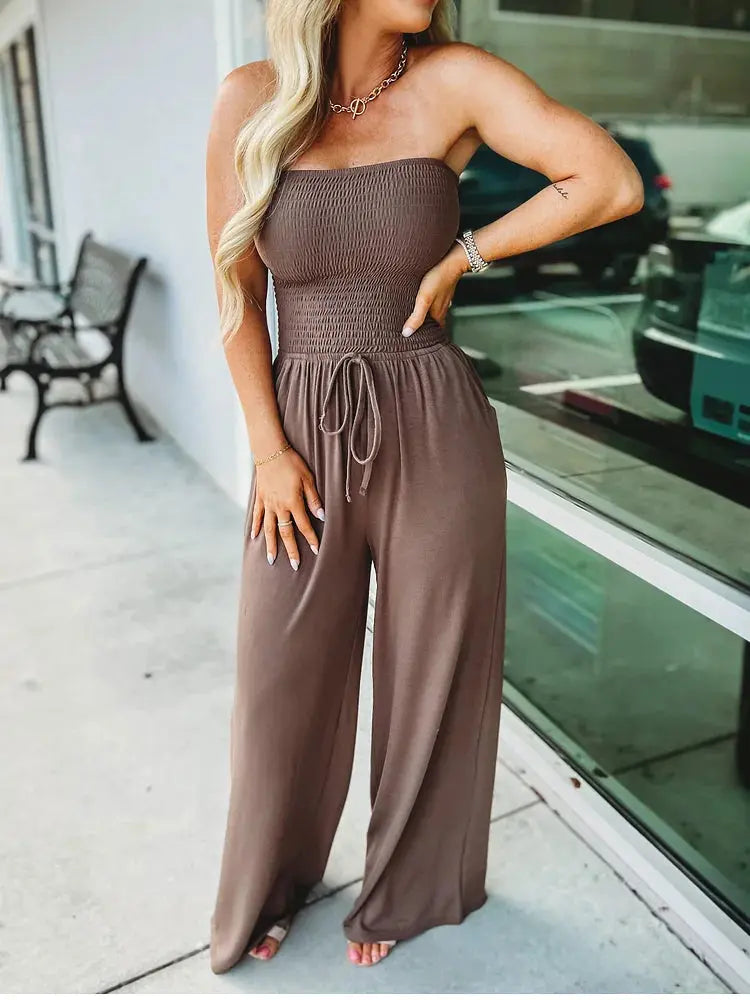 Donna con tuta marrone senza spalline, pantaloni larghi, posa all'aperto. Moda estiva, abbigliamento casual elegante, tendenza femminile 2023.