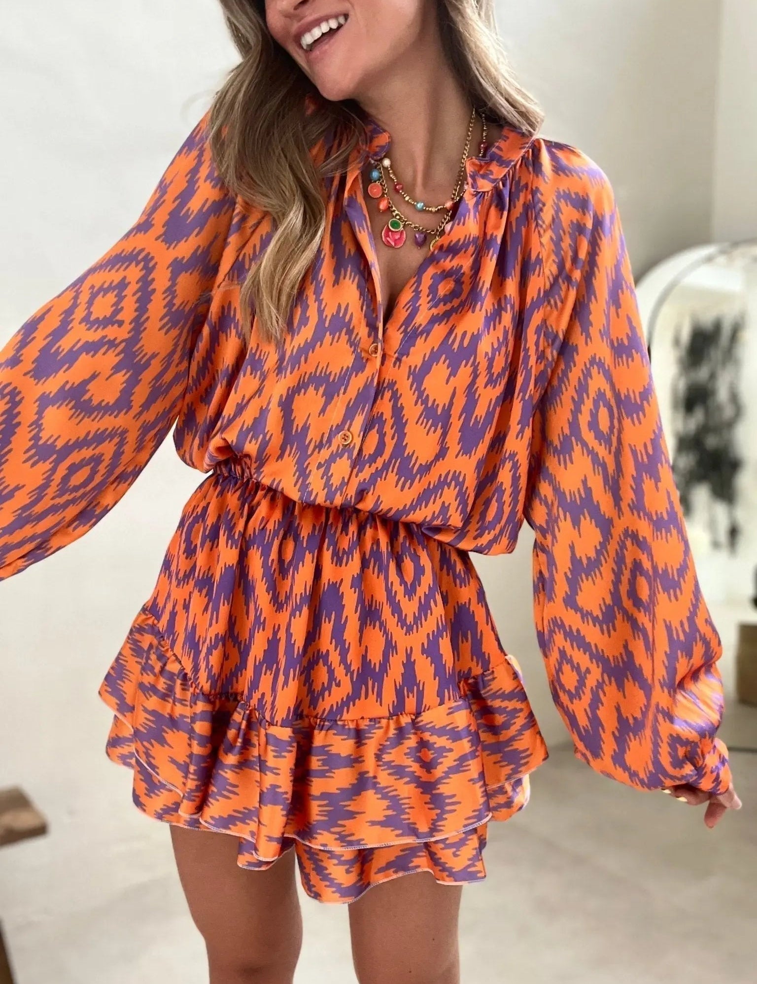 Abito donna a fantasia ikat arancione e viola, maniche lunghe, scollo a V, gonna a balze. Moda femminile, abbigliamento estivo elegante.