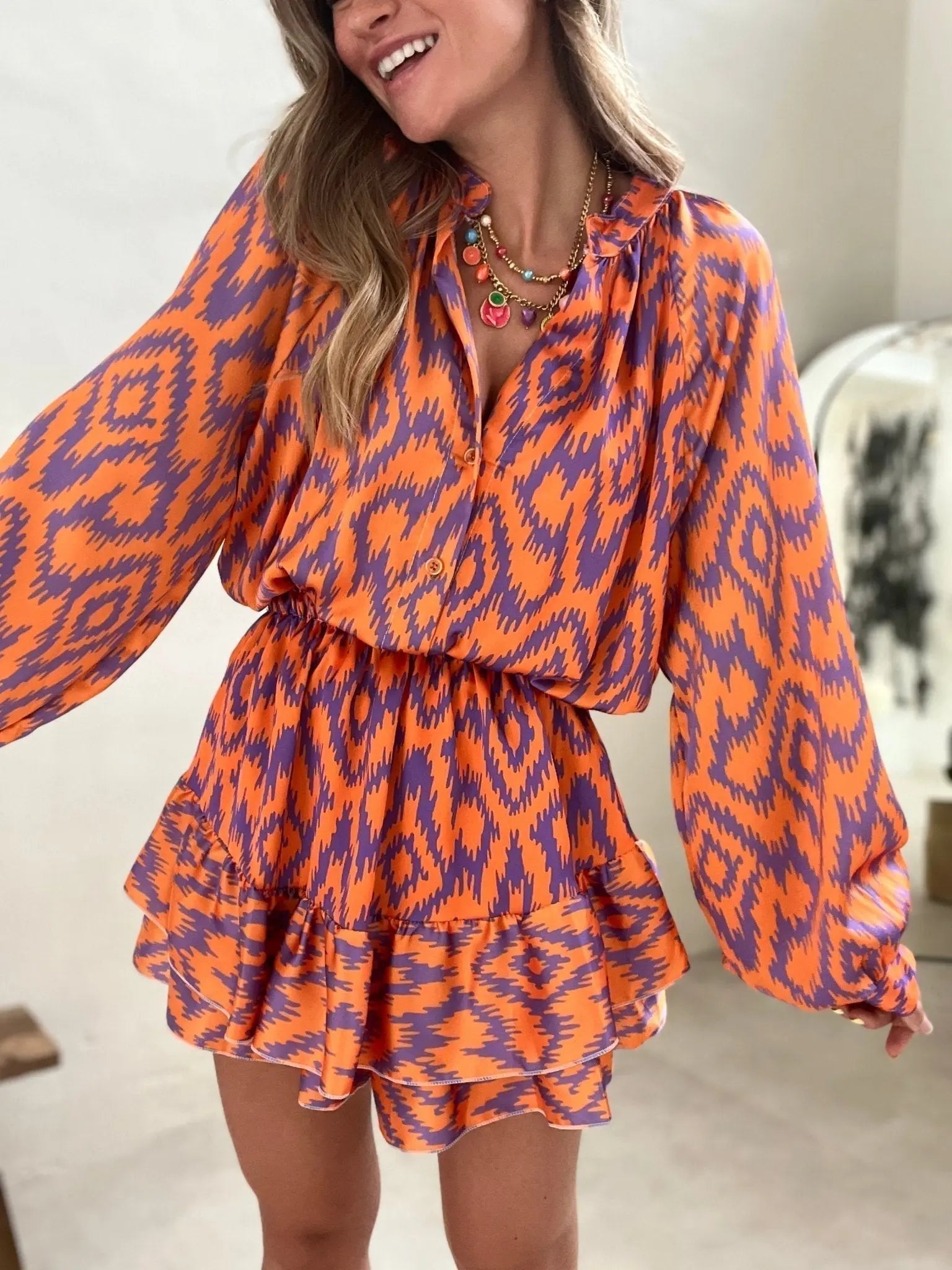 Abito donna a fantasia ikat arancione e viola, maniche lunghe, scollo a V, gonna a balze. Moda femminile, abbigliamento estivo elegante.