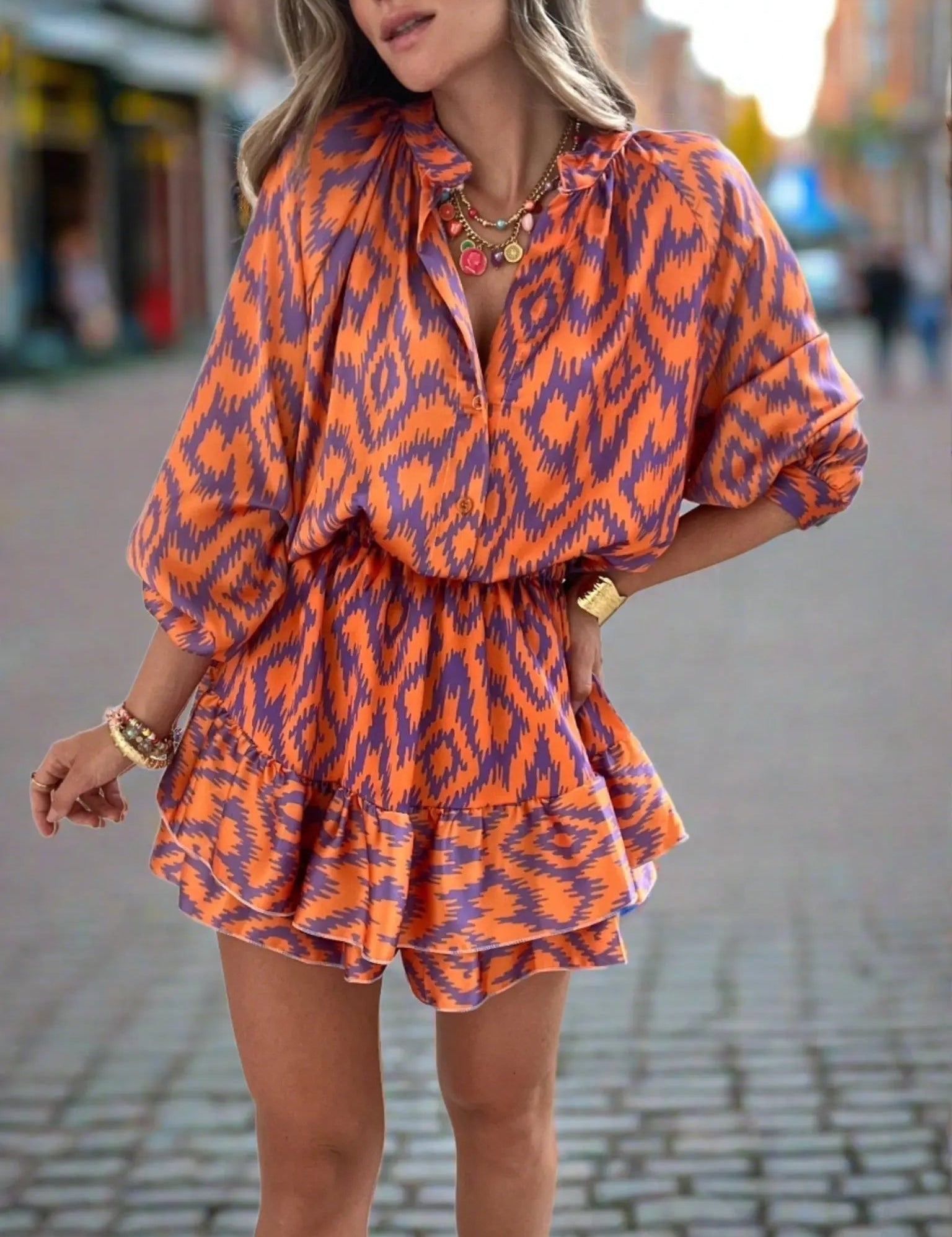 Abito corto donna arancione e blu con motivo ikat, maniche lunghe, scollo a V, indossato in strada. Moda femminile, abbigliamento estivo elegante.