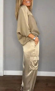Donna in abbigliamento casual beige, camicia oversize e pantaloni cargo satinati, posa sorridente. Moda femminile elegante e confortevole.