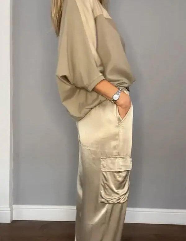 Donna in abbigliamento casual beige, camicia oversize e pantaloni cargo satinati, posa sorridente. Moda femminile elegante e confortevole.