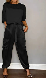 Donna in tuta nera elegante con tasche cargo, maniche lunghe, abbinata a tacchi leopardati. Look moda casual chic per eventi serali.