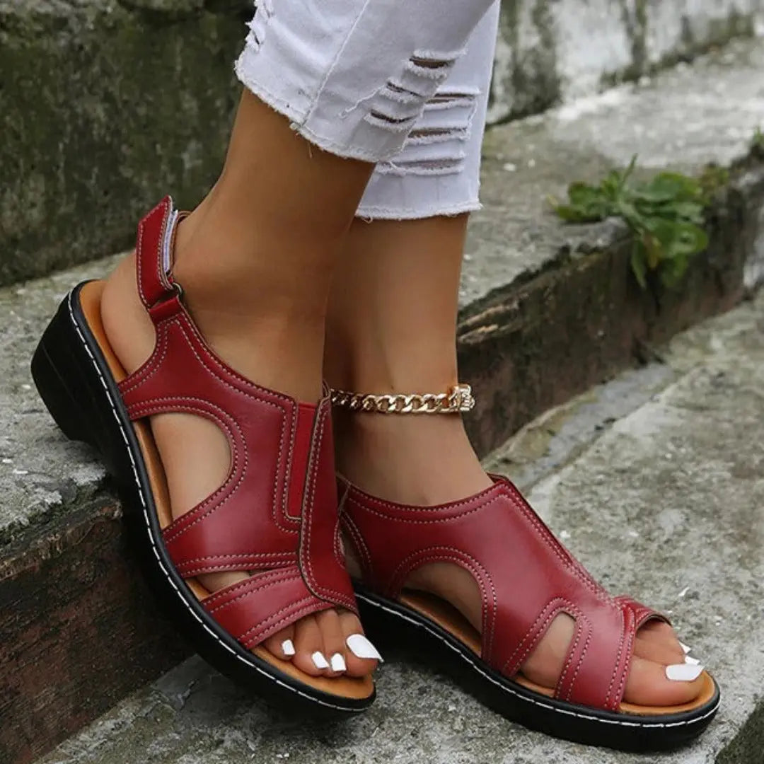 Sandali rossi in pelle da donna, con tacco basso e cinturino alla caviglia, indossati con jeans bianchi strappati. Scarpe estive eleganti.