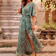Abito lungo estivo verde con stampa floreale, scollo a V e spacco laterale, indossato da donna su gradini in pietra, moda femminile elegante.