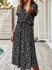Abito lungo nero a pois bianchi, maniche corte, scollo a V, stile casual estivo, indossato da donna su terrazza. Moda femminile elegante.