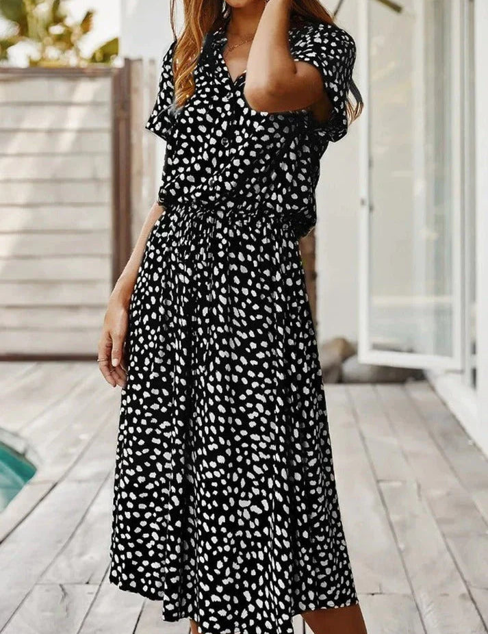 Abito lungo nero a pois bianchi, maniche corte, scollo a V, stile casual estivo, indossato da donna su terrazza. Moda femminile elegante.