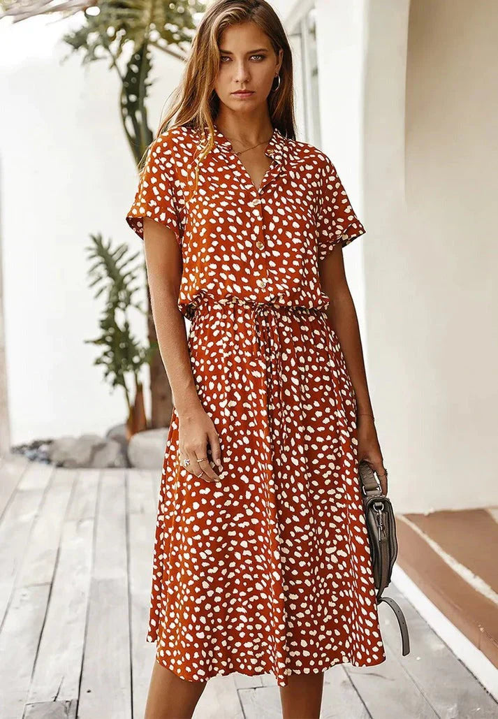 Abito estivo donna a pois bianchi su sfondo arancione, maniche corte, lunghezza media, cintura in vita, moda casual, perfetto per giornate calde.