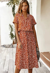 Abito estivo donna a pois bianchi su sfondo arancione, maniche corte, lunghezza media, cintura in vita, moda casual, perfetto per giornate calde.